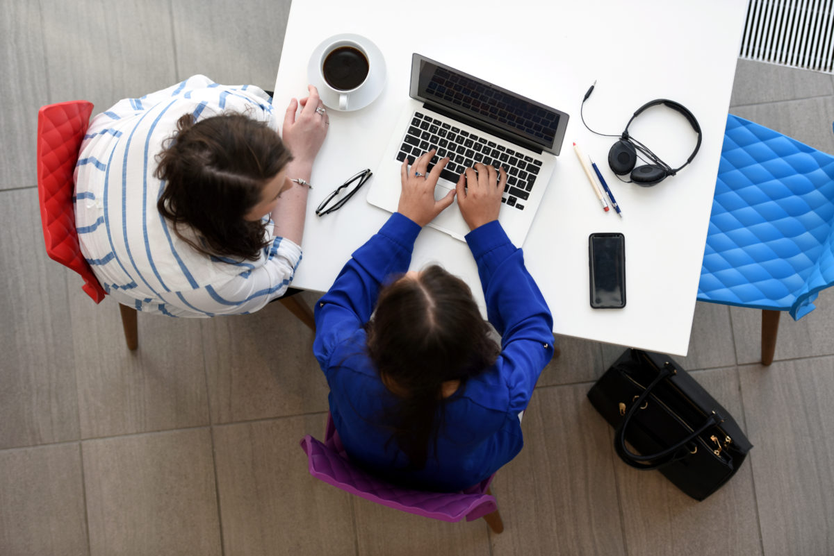 Two people sitting at a table looking at a laptop.